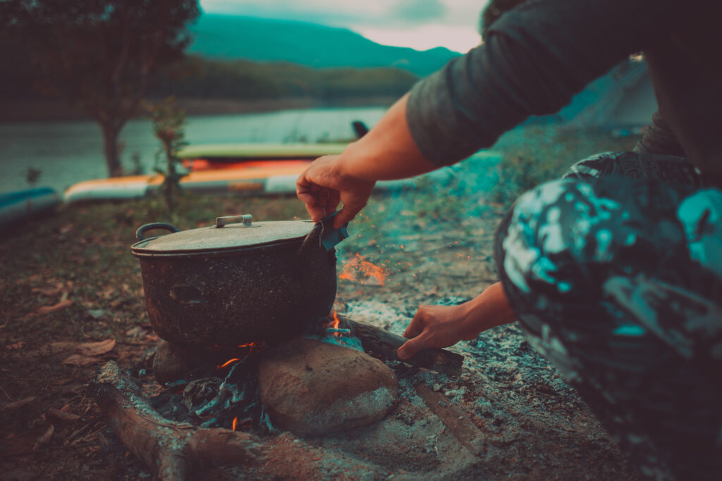 A person cooking over a campfire with coals and stones.