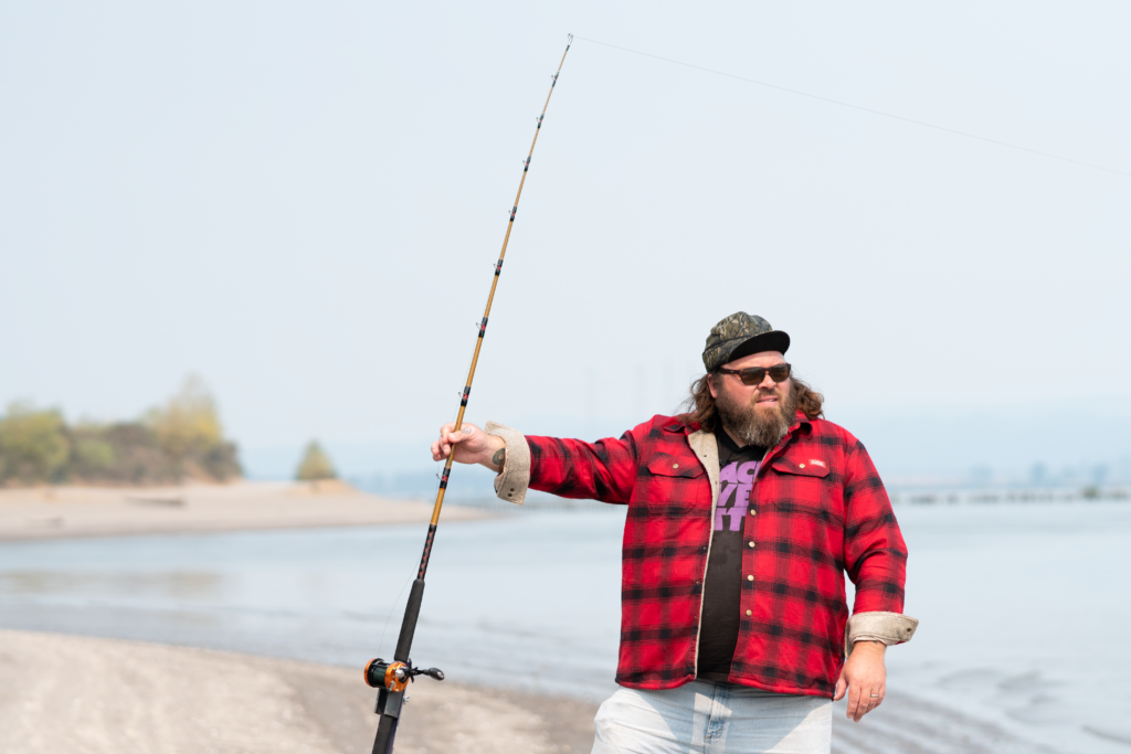 Nate P. (@shorelunch_with_nate_p) stands on the beach with his fishing pole.