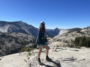 Laura Brouwer (@brouwerl) stands on a rocky path overlooking a beautiful mountain view.