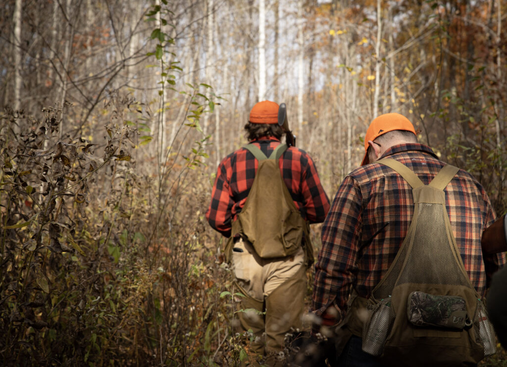 two men walk with their backs to the camera through the woods.