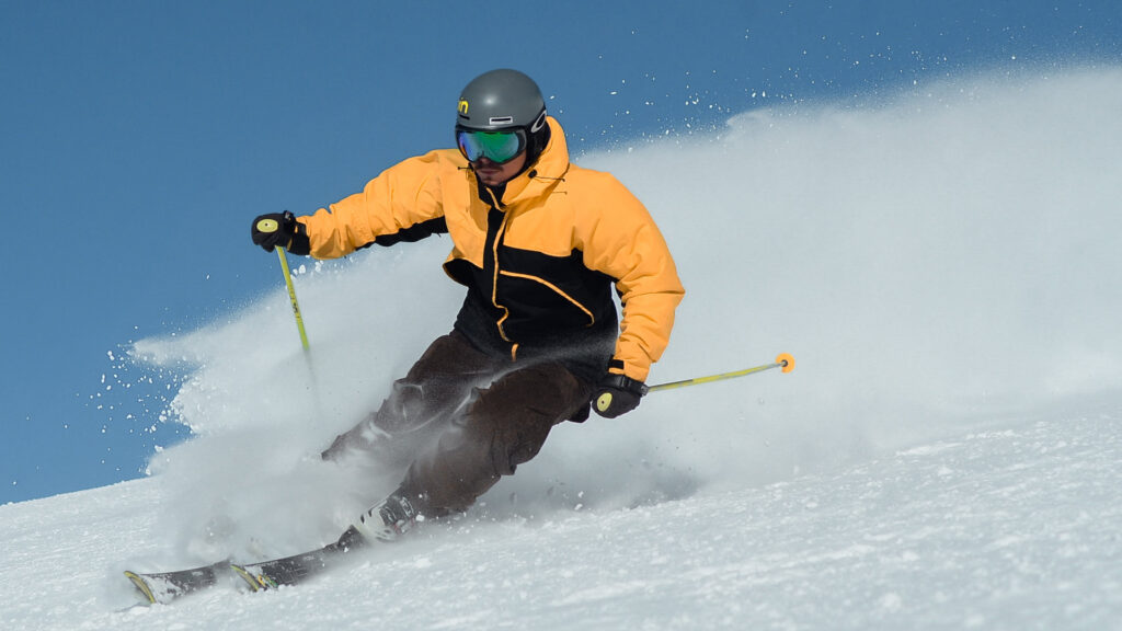 a skier in a yellow jacket going down hill on a clear day