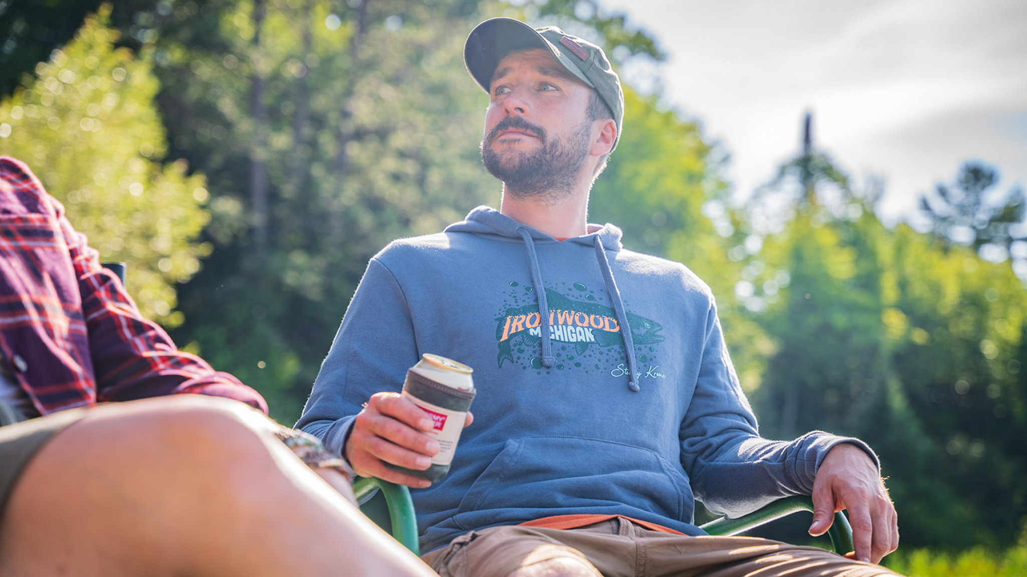 SK Terry Hoodie Spring Launch a guy sitting around a campfire with a canned drink