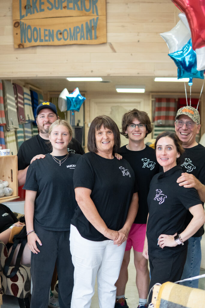 The Lake Superior Woolen Company team smiles in front of the company sign.